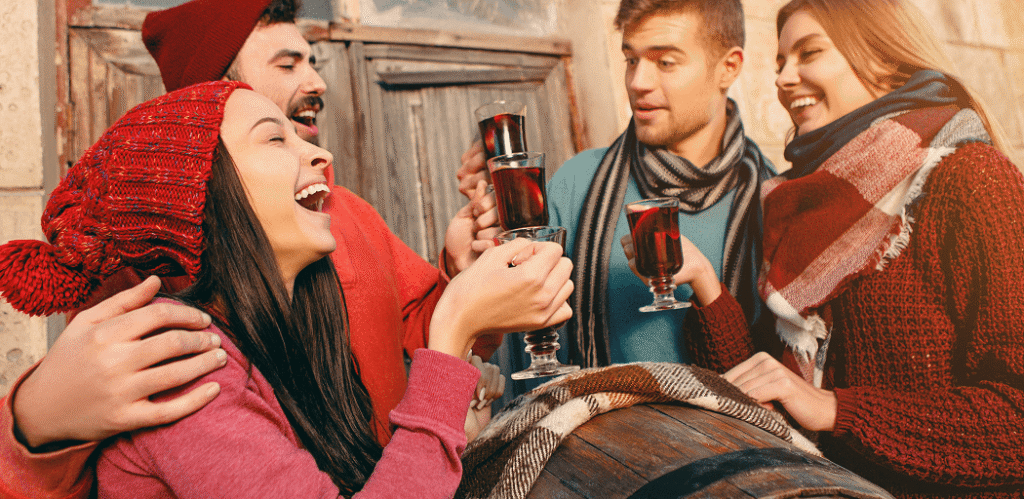 Group of people in winter clothes enjoying wine around a barrel in a rustic outdoor setting