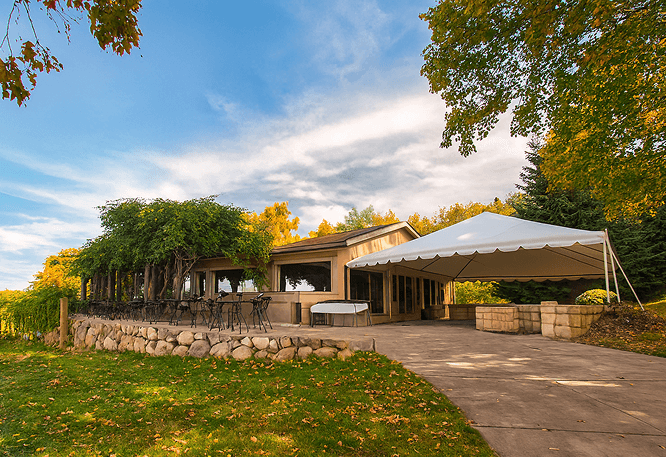 Outdoor patio with tent and chairs surrounded by trees.
