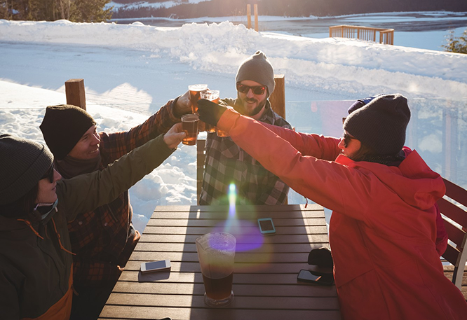 People toasting drinks at a snowy mountain table with scenic views.