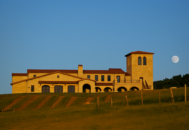 Elegant hillside villa with arches and tower under moonlit blue sky, surrounded by grassy lawn and scenic tranquility.