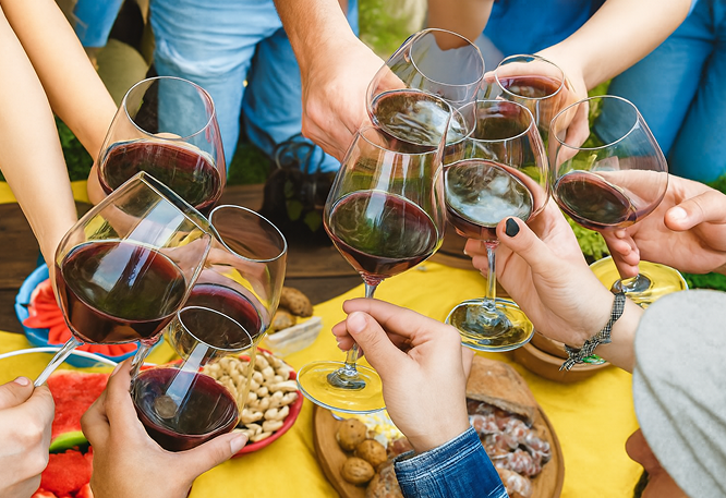  Group of people toasting with glasses of red wine over a table with snacks on a yellow cloth