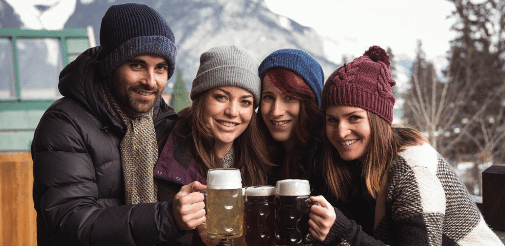 Group of friends toasting with red wine at an outdoor winter gathering, surrounded by festive food and snow-covered trees.